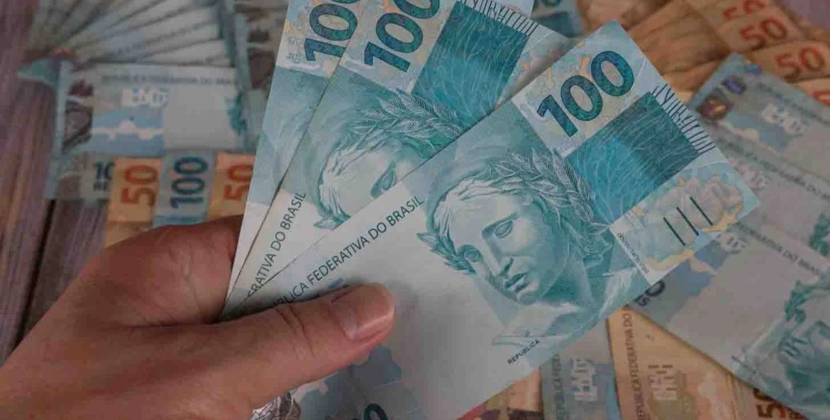 Mão segurando três notas de 100 R$