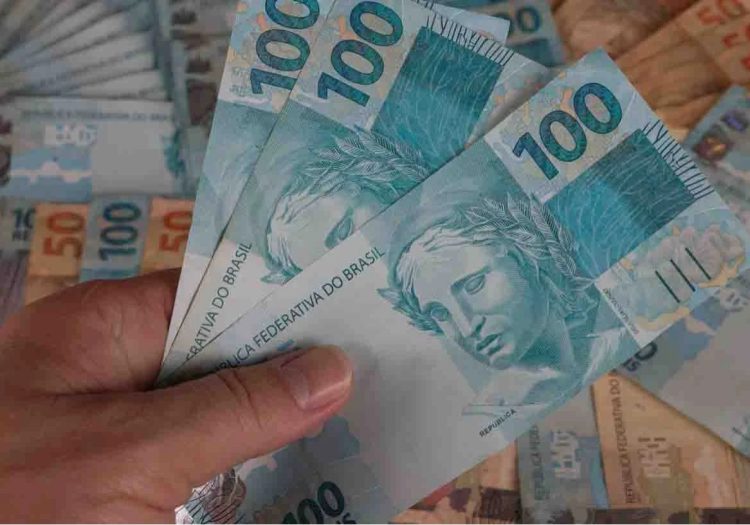 Mão segurando três notas de 100 R$